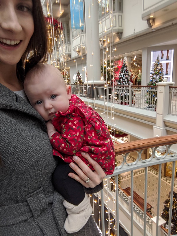 Quinn is held by her mom in a mall decorated for Christmas